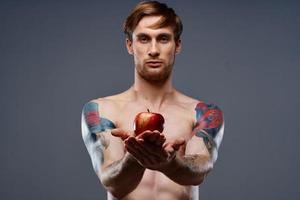 tätowiert Athlet halten rot Apfel auf grau Hintergrund nackt Torso abgeschnitten Aussicht foto