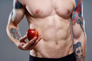 männlich Athlet mit ein Apfel im seine Hände und tätowieren Würfel auf seine Bauch Bizeps Drücken Sie foto