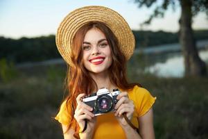 Frau im ein Hut mit ein Kamera im ihr Hände rot Lippen attraktiv aussehen Natur foto