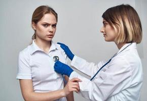 Arzt Frau mit ein Stethoskop hält ein geduldig durch das Schulter auf ein Licht Hintergrund foto