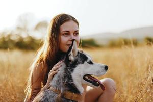 Frau und ihr heiser Hund glücklich Bummel durch das Gras im das Park Lächeln mit Zähne fallen Sonnenuntergang gehen mit Haustier, Reise mit ein Hund Freund foto