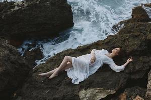 Frau im lange Weiß Kleid nass Haar Lügen auf ein felsig Cliff Ferien Konzept foto