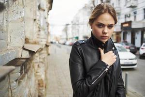 Frau Gehen Nieder das Straße in der Nähe von das Gebäude im Leder Jacke abgeschnitten Aussicht foto