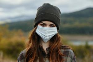 Frau mit ein medizinisch Maske auf ihr Gesicht und im ein warm Hut im ein Plaid Hemd Herbst Natur foto