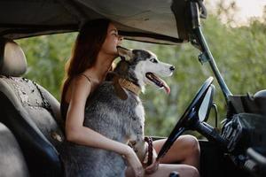 ein schön jung Frau sitzt hinter das Rad von ihr Auto zusammen mit ein heiser Rasse Hund und lächelt fröhlich genießt das Reise foto