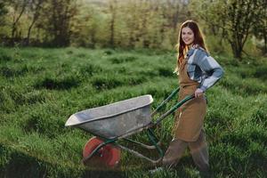 ein glücklich Frau mit ein Wagen funktioniert im ihr Land Zuhause im das Landschaft gegen ein Hintergrund von Grün Gras und Sonnenuntergang Sonne foto