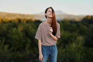 ein jung Frau lacht und sieht aus beim das Kamera im einfach Kleider gegen das Hintergrund von ein schön Landschaft von Berge und Bäume im Herbst foto