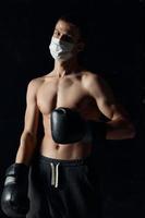 Bodybuilder Boxer im ein medizinisch Maske auf ein schwarz Hintergrund Handschuhe Athlet nackt Torso foto