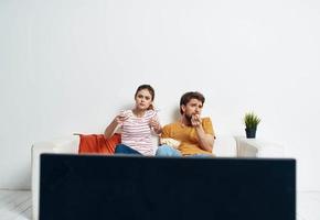 ein Mann und ein Frau sind Sitzung auf das Couch im Vorderseite von das Fernseher und ein Grün Blume im ein Topf drinnen foto