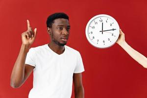 Mann von afrikanisch Aussehen Nächster zu das Uhr Zeit Emotionen rot Hintergrund foto