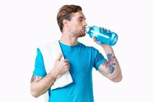 Sport Kerl im Blau T-Shirt mit ein Flasche von Wasser im das Fluss und tätowieren Weiß Hintergrund Fitness Modell- foto