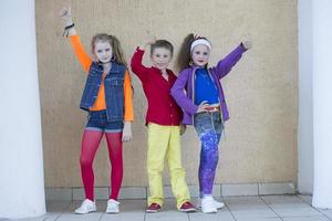 Kinder Pose zum ein Foto schießen. Junge und zwei wenig Mädchen Modelle im hell Kleider sind suchen beim das Kamera.