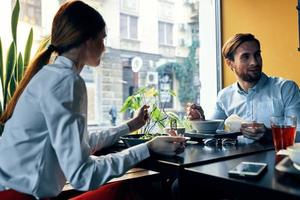 ein Mann und ein Frau im ein Hemd haben Abendessen beim ein Tabelle im ein Restaurant Innere im das Hintergrund heiß Essen Getränke foto
