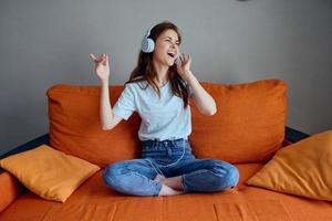 ziemlich Frau Sitzung auf das Couch beim Zuhause Hören zu Musik- auf Kopfhörer Wohnungen foto