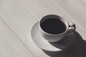 schwarz Kaffee im Weiß Tasse mit ein Untertasse auf Licht hölzern Tisch, Schatten, Kopieren Raum foto