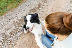 lächelnde junge attraktive Frau, die mit niedlichem Hündchen-Border-Collie auf sommerlichem Hintergrund im Freien spielt. mädchen, das einen umarmenden hundefreund hält. Haustierpflege und Tierkonzept. foto