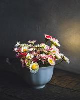 Strauß gewöhnlicher Gänseblümchen im Tee, der im glühenden Licht des frühen Morgens auf Holztisch geschnitten wird foto
