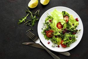 frische grüne gemischte Salatschüssel mit Tomaten und Mikrogrün auf schwarzem Betonhintergrund foto