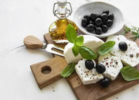 frischer Ricotta mit Basilikumblättern und Oliven auf einem Holzbrett foto