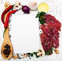 Fleischsteaks, ein Rezeptbuch und Zutaten auf einem alten hölzernen Hintergrund foto