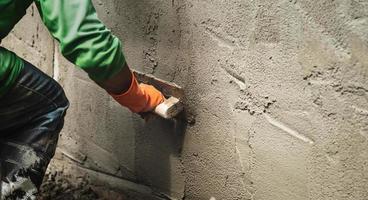 Nahansicht Hand Arbeiter Verputzen Zement auf Mauer zum Gebäude Haus foto