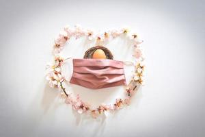 Frühlingsgänseblümchen blüht in Form eines Herzens mit rosa Maske, die ein Osterei bedeckt foto