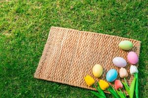 glücklich Ostern Urlaub Gruß Karte Konzept. bunt Ostern Eier und Frühling Blumen auf Papyrus Rattan weben Textur Hintergrund. eben legen, oben Sicht, Kopieren Raum. foto