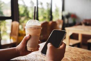 Frau Hand halten Kaffee im Plastik Tasse und Handy, Mobiltelefon Telefon im Geschäft foto