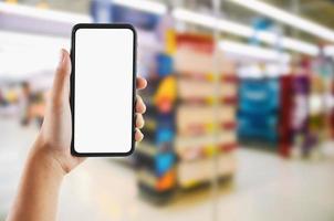 Hand halten Handy, Mobiltelefon Weiß Bildschirm auf Supermarkt Geschäft verwischen Hintergrund foto