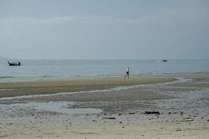 gesund Mann läuft allein entlang das Strand mit horizontal Linie von Seelandschaft und Parkplatz Boote im Hintergrund foto