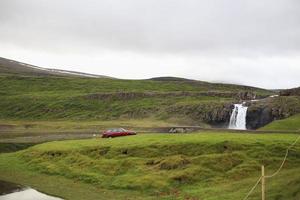 einsames rotes Auto in der Nähe eines Wasserfalls in Island geparkt foto