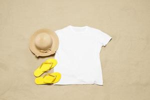 Sand Strand Textur Hintergrund. Attrappe, Lehrmodell, Simulation Weiß Sommer- T-Shirt Kopieren Raum. leer Vorlage Frau Hemd oben Sicht. Sommer Zubehör Hut, Flip-Flops. flach liegen Nahansicht T-Shirt auf Strand. Strandzeit foto