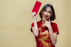 Porträt schön asiatisch Frau im cheongsam Kleid, Thailand Leute, glücklich Chinesisch Neu Jahr Konzept, glücklich asiatisch Dame im Chinesisch traditionell Kleid halten ein rot Briefumschlag foto