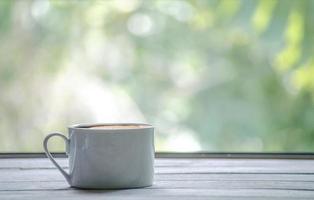 heiße weiße Kaffeetasse auf einem Holztisch und grünem Blatthintergrund mit Kopienraum foto