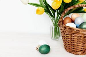 Strauß von Gelb Tulpen und Ostern Eier im ein Korb auf ein Licht Hintergrund foto