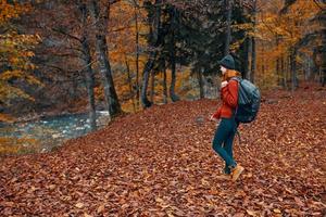 Frau im Herbst im das Park mit gefallen Blätter und ein Rucksack auf ihr zurück Fluss im das Hintergrund foto