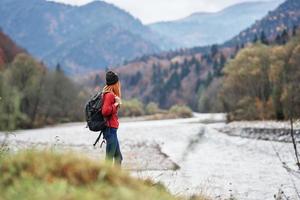 jung Reisender mit ein Rucksack im Jeans und ein Sweatshirt in der Nähe von das Fluss im das Berge foto