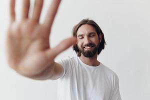 glücklich Erwachsene Mann mit ein Bart lächelt und zieht das Koch in das Kamera Hören zu Musik- im Kopfhörer im ein betrübt T-Shirt auf ein Weiß isoliert Hintergrund foto