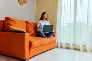 ziemlich Frau mit lange Haar Lügen auf das Couch mit ein Laptop Wohnungen foto