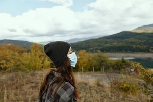 Frau im warm Kappen im das Herbst Wald mit ein medizinisch Maske auf ihr Gesicht foto