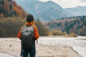 Frau Reisen im das Berge im Herbst in der Nähe von das Fluss im Natur mit ein Rucksack zurück Aussicht foto