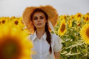 schön Süss Mädchen im ein Stroh Hut im ein Weiß Kleid ein Feld von Sonnenblumen Landwirtschaft Sommer- Zeit foto