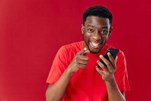 heiter Mann von afrikanisch Aussehen mit Handy, Mobiltelefon Telefon Lachen auf rot Hintergrund foto