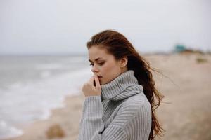 Porträt von ein Frau rot Haar im ein Sweatshirt durch das Ozean unverändert foto