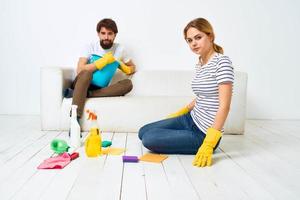 Frau wäscht das Böden ein Mann sitzt auf das Couch beim Zuhause Innere Reinigung foto