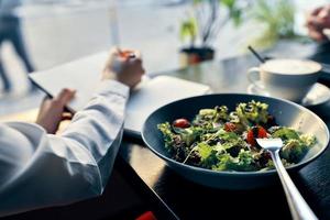 köstlich Essen Salat im ein Teller Gabel Notizblock mit das Inschrift und Frau im Hemd Cafe Innere foto