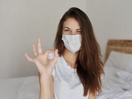 Frau auf Sitzung auf Bett tragen medizinisch Maske positiv Hand Geste foto