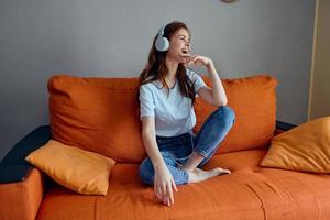 Frau Hören zu Musik- mit Kopfhörer auf das Orange Sofa Lebensstil foto