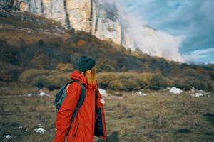 Frau im Jacken Kappen mit ein Rucksack auf ihr zurück Spaziergänge im das fallen im das Berge und im Natur foto