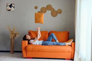 lächelnd Frau auf das Orange Couch im das sich ausruhen Zimmer posieren Wohnungen foto